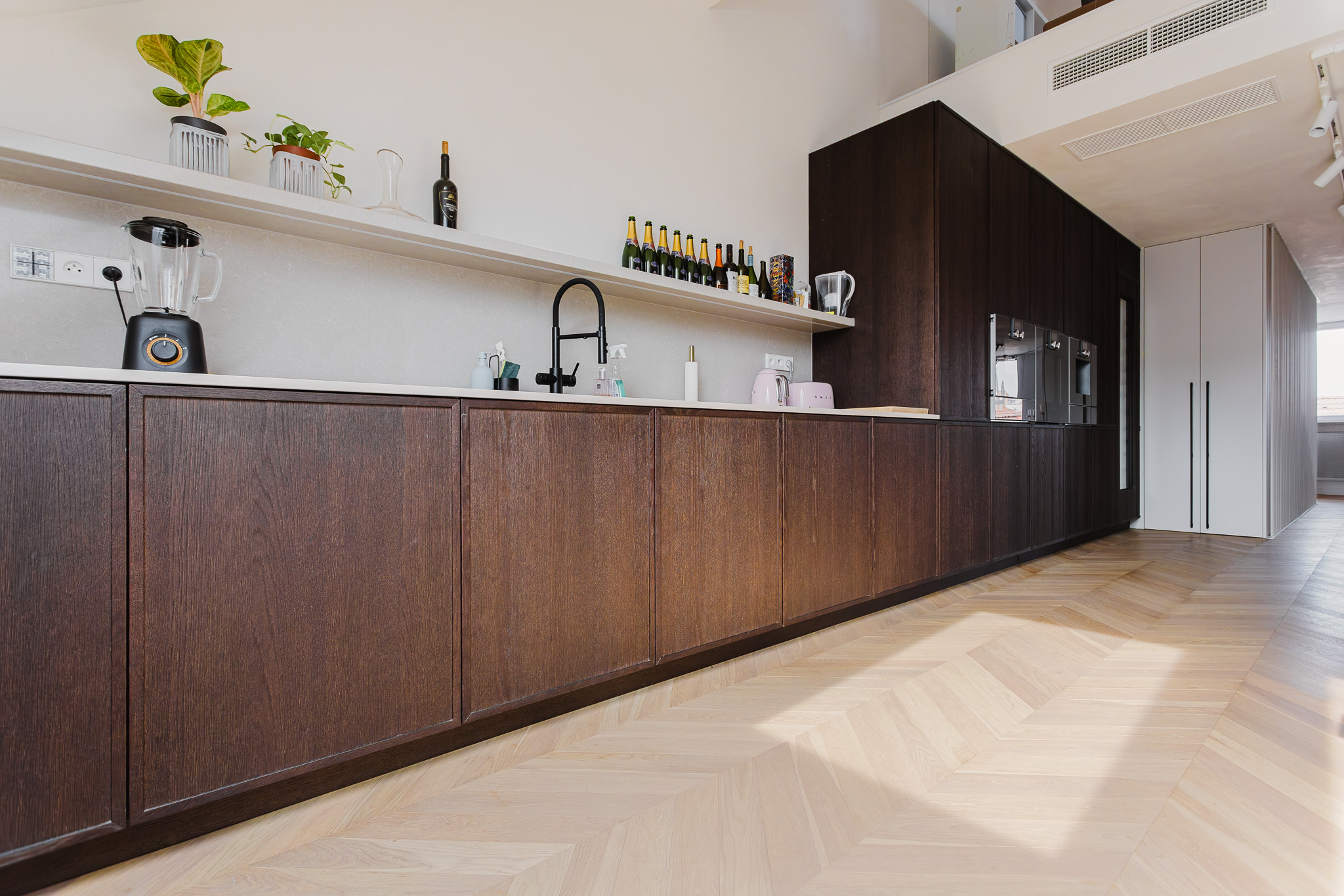 Moderna kuhinja z elegantnimi temnimi omaricami in svetlim ribja kost parketom v prostorih z naravno svetlobo.